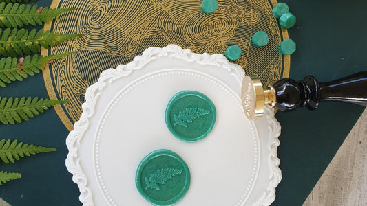 white wax seal on pink envelope with brass wax seal stamp