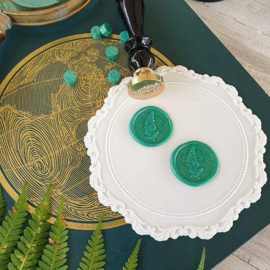 Fern wax seal stamp with black handle and green fern wax seals on white wax sealing mat with wax sealing beads