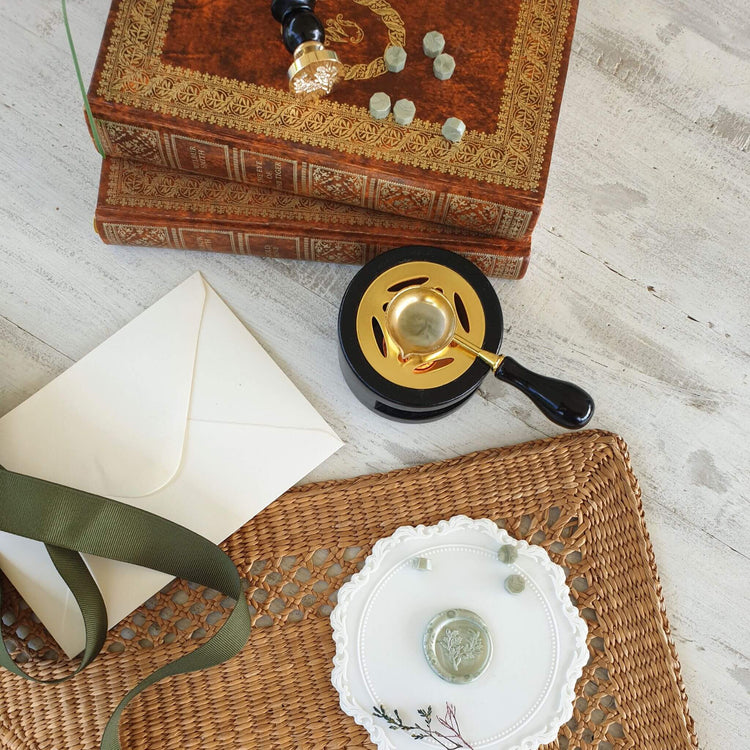 black and gold wax melter with wax melting spoon and sage green wax sealing beads with a foliage wax seal