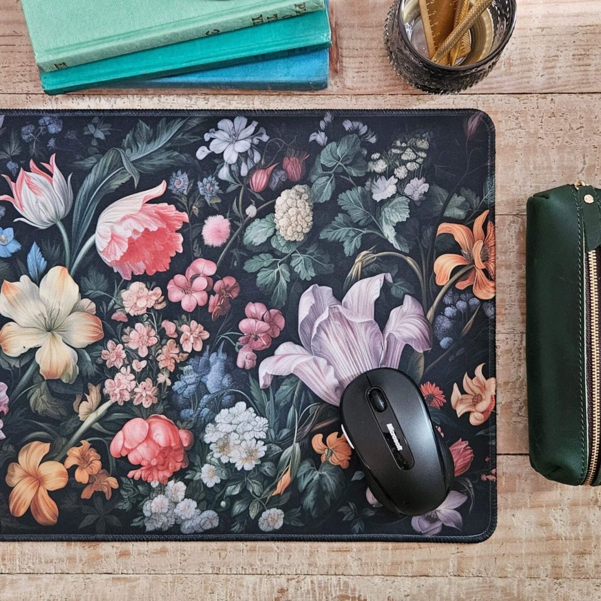 Large floral mouse pad on a wood desk with a mouse, vintage books, and a pencil pouch.