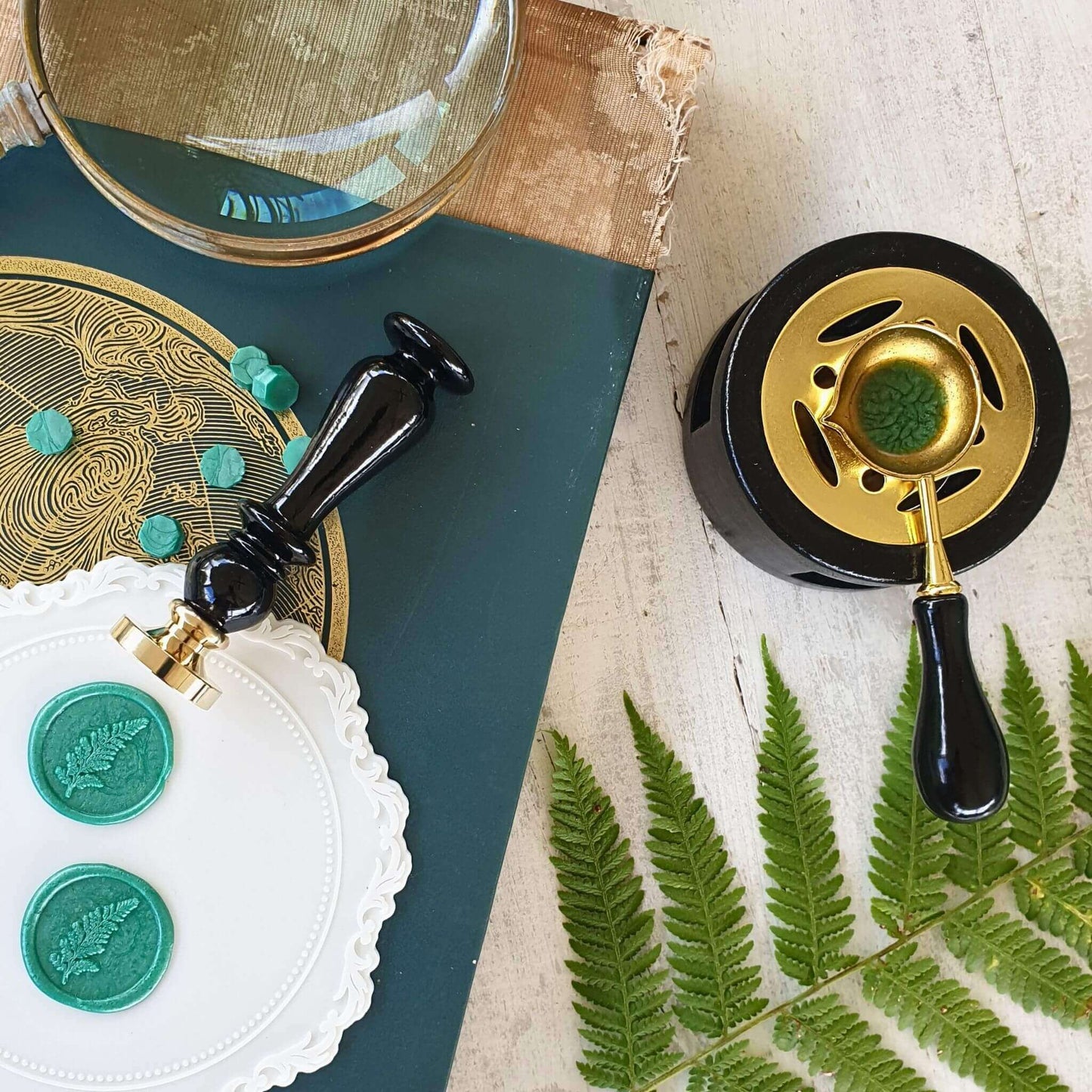 overhead image of wax melting stove and spoon in use with green sealing wax and fern wax seal stamp