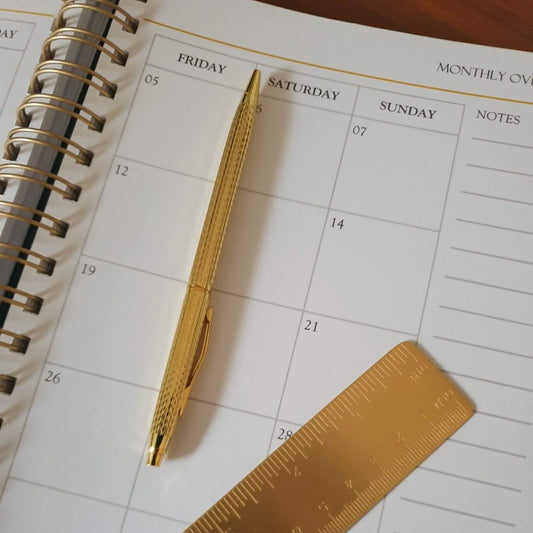 gold pen on planner with gold ruler