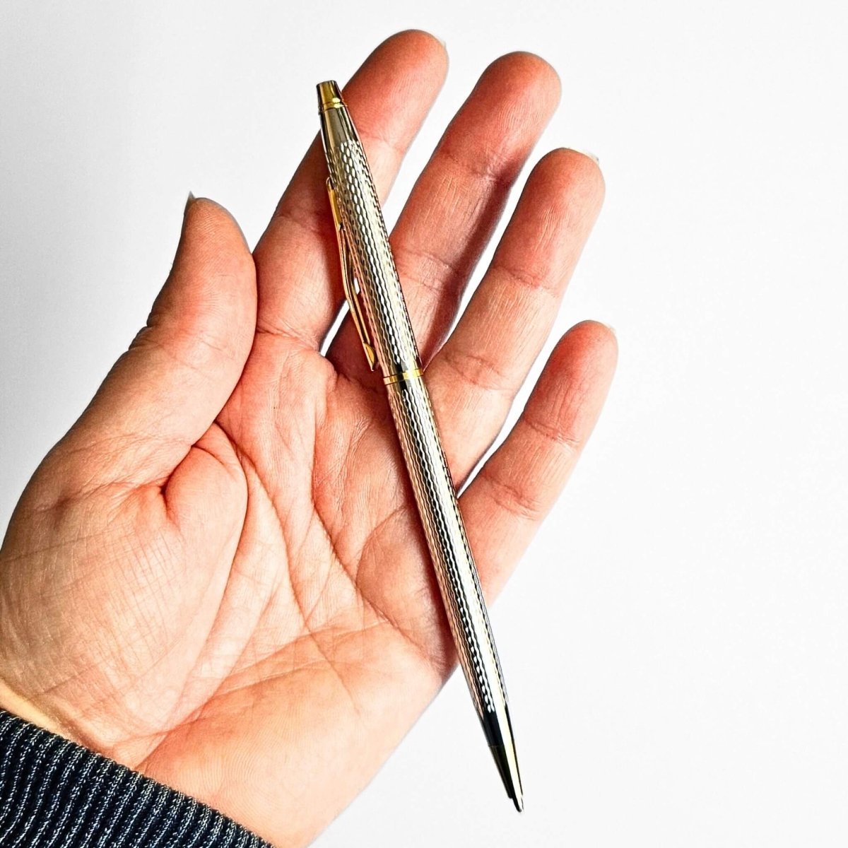 Hand holding a silver pen with a gold clip against a white background