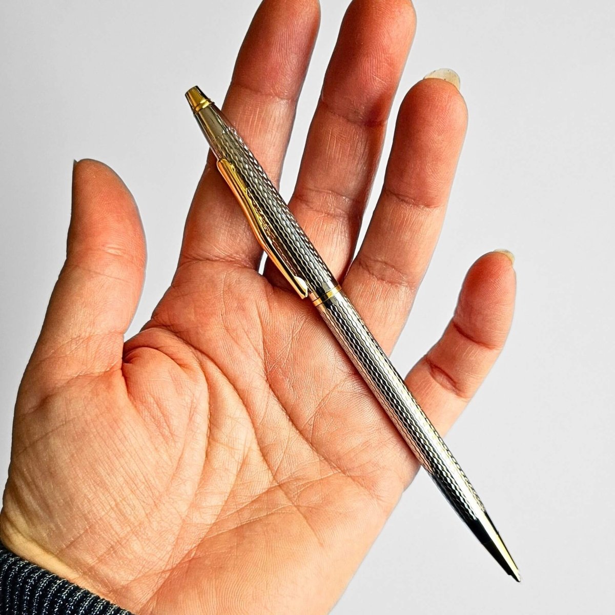 Hand holding a silver pen with a gold clip against a plain background