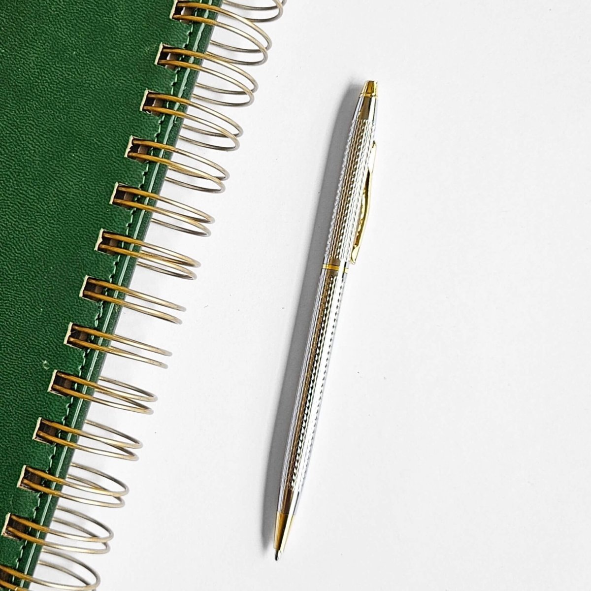 Green notebook with gold spiral binding and a matching pen on a white background