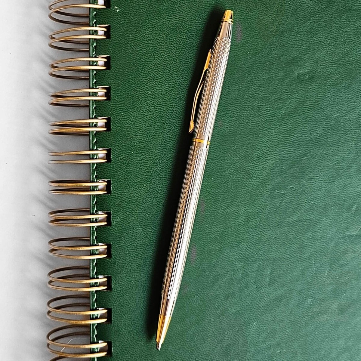 Silver and gold pen on a green notebook with gold spiral binding