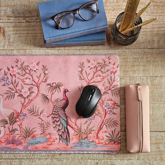 Pink floral mouse pad with a mouse, glasses, books, and a pencil holder on a wooden desk.