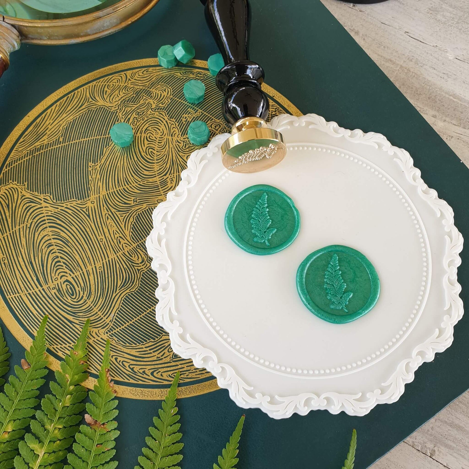 Fern wax seal stamp with green wax seals and sealing wax beads on white silicone mat
