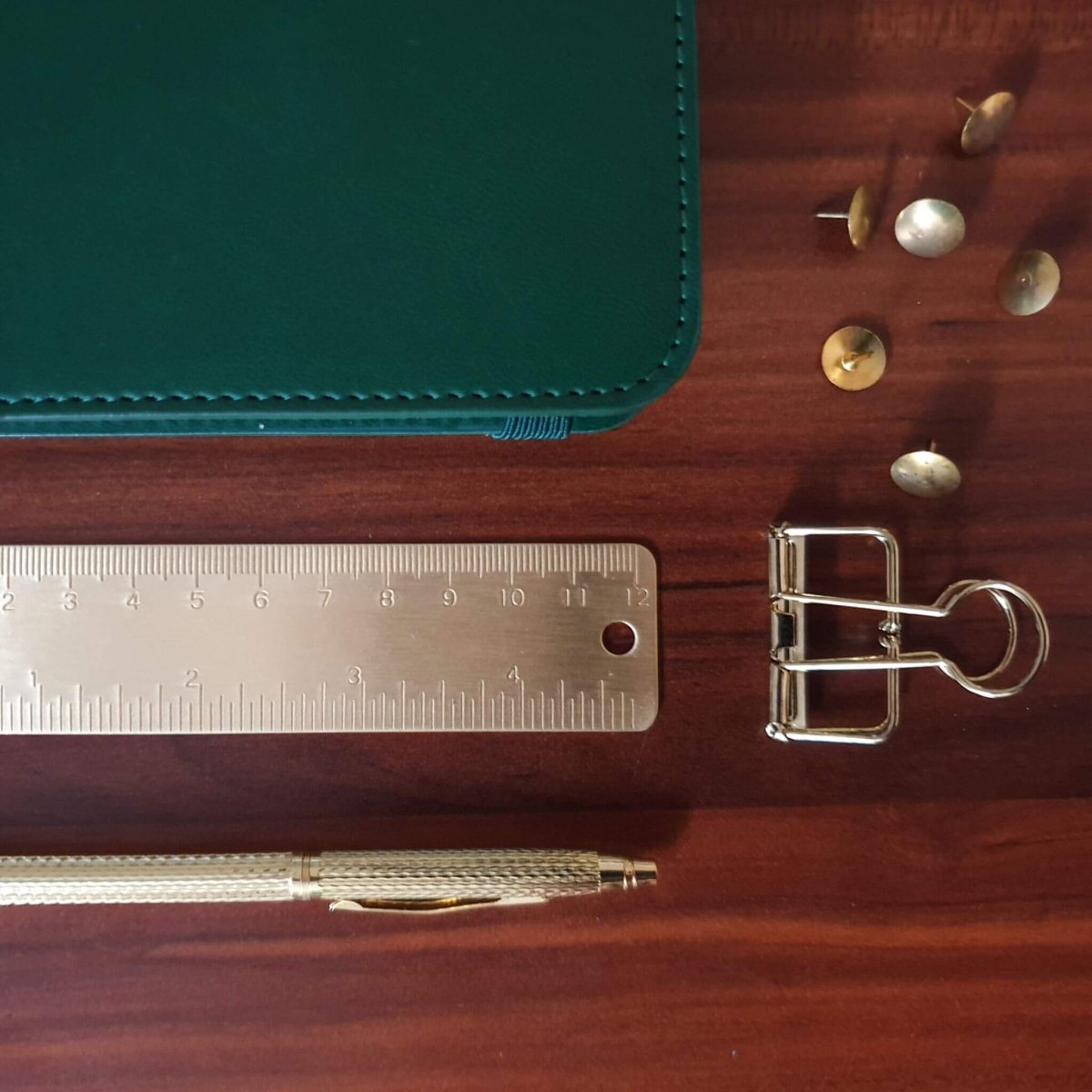 stationery flatlay with brass ruler, gold pen , planner and clips