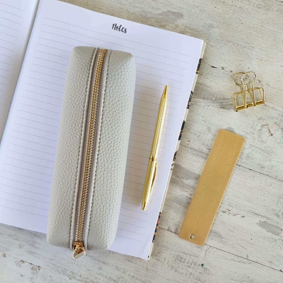light grey pencil case on notebook with gold stationery