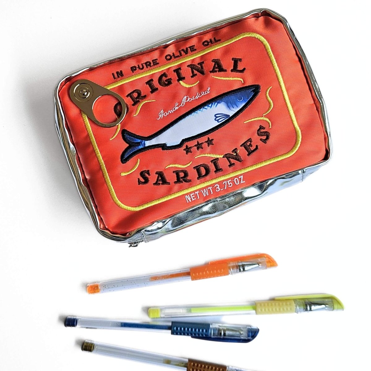 Orange sardine can-shaped pencil case with pens on a white background
