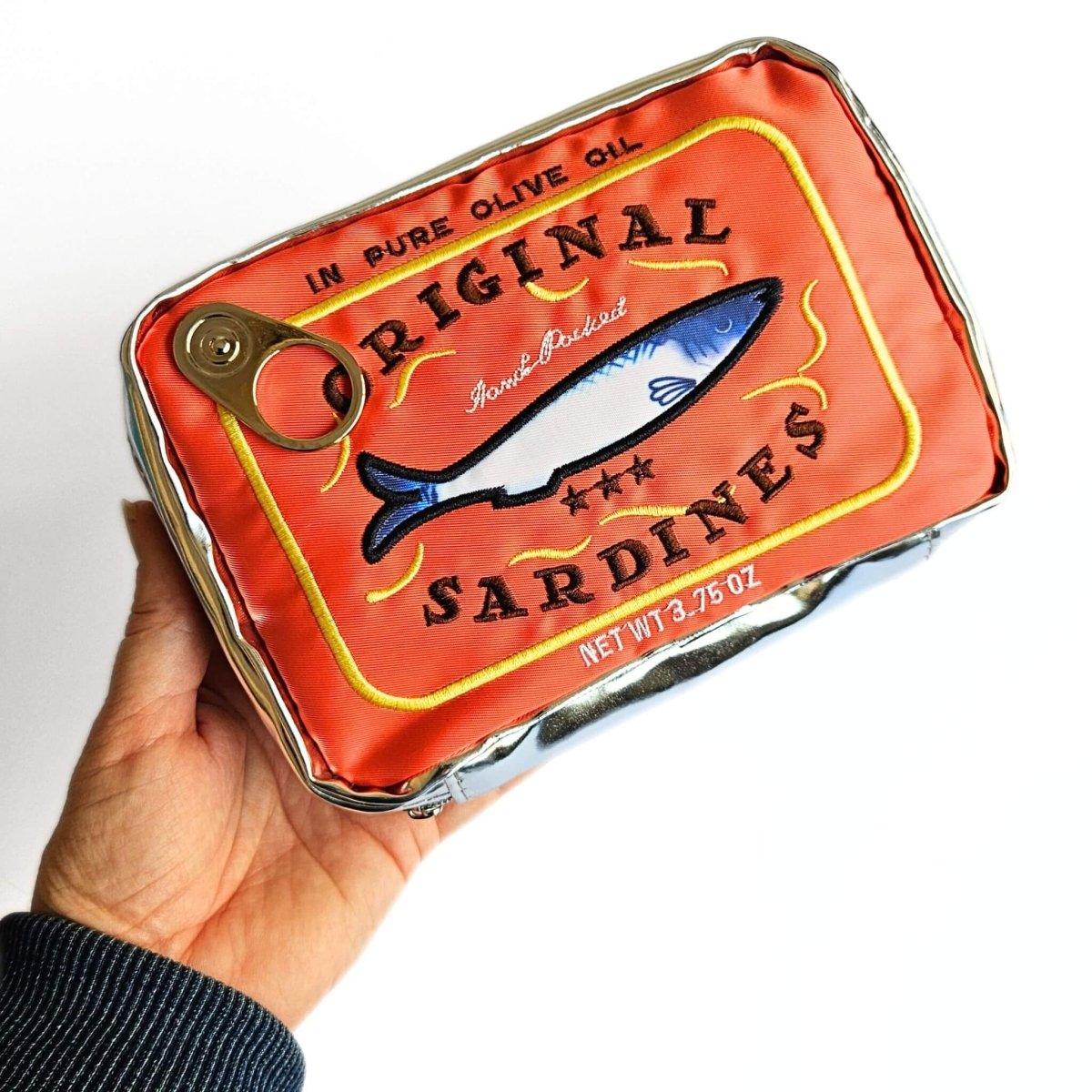 Hand holding an orange-red sardine tin pencil case with a fish illustration on a white background