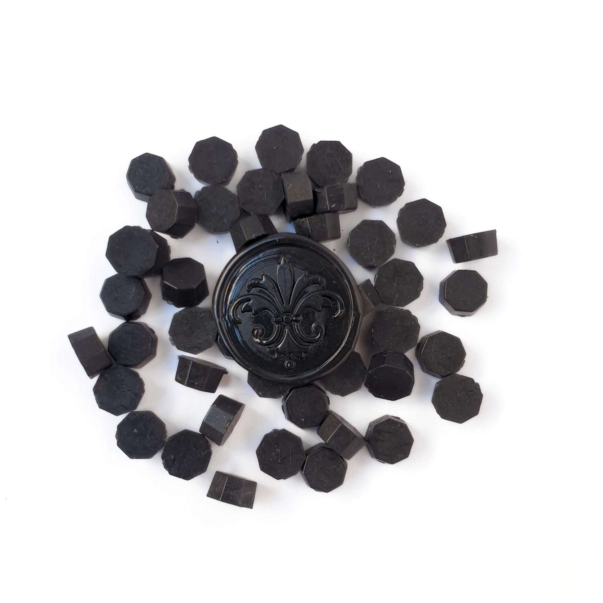 Black octagonal shaped sealing wax beads scattered, with a black wax seal in the middle
