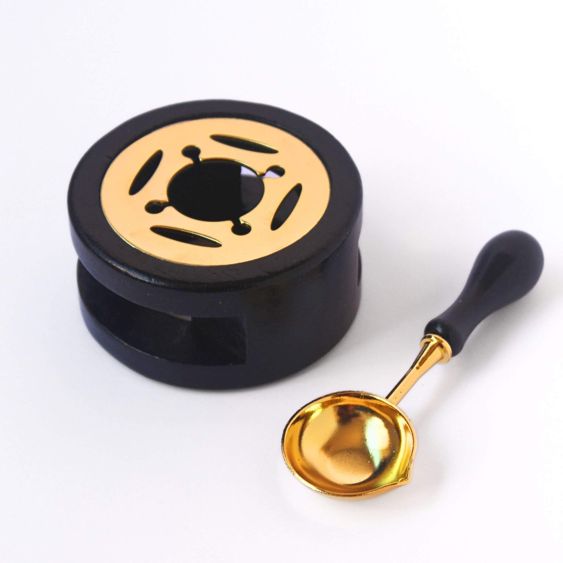 Black wax melting furnace with gold detail and matching black and gold wax melting spoon beside it