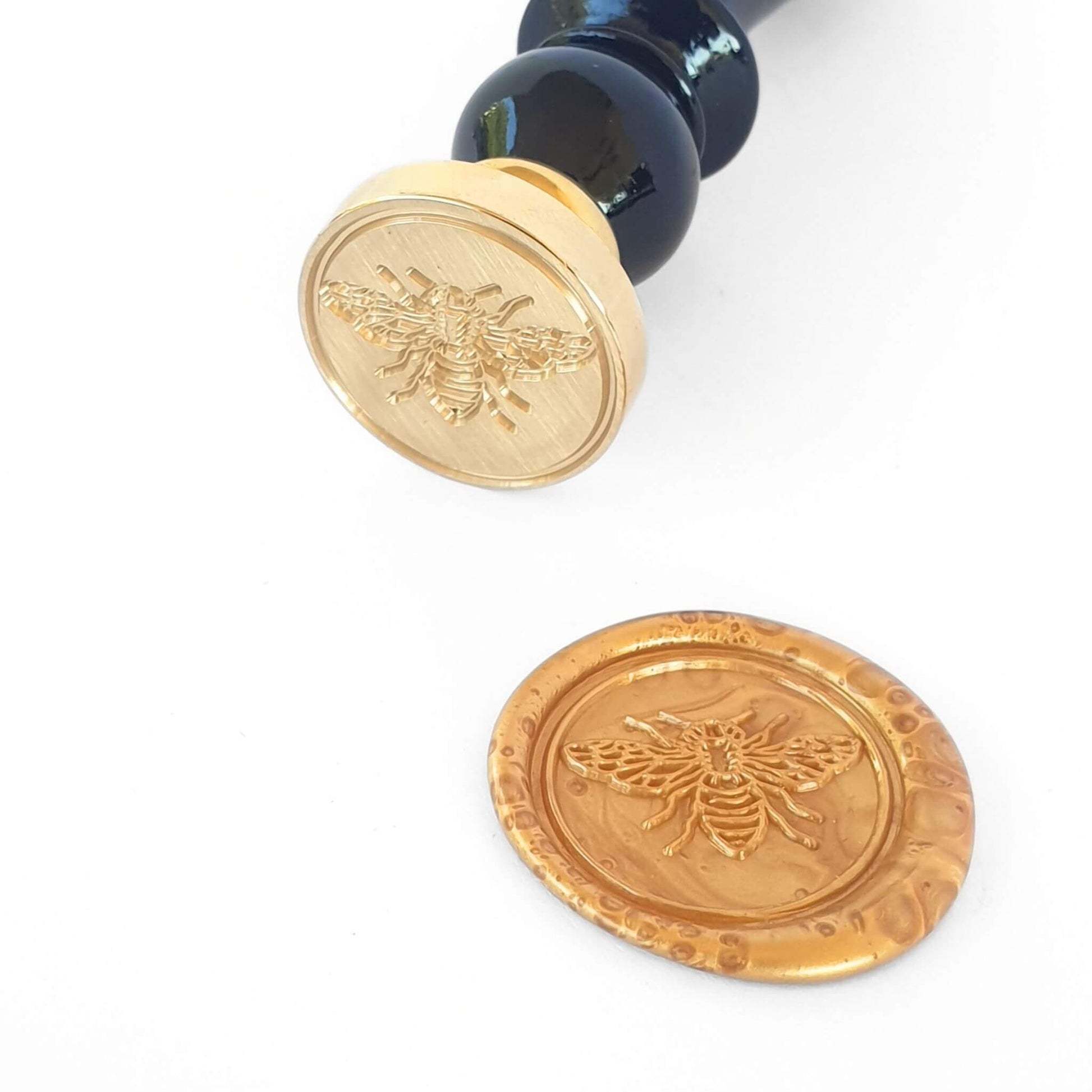 Wax Seal with bumble bee design and black handle next to gold bee wax seal