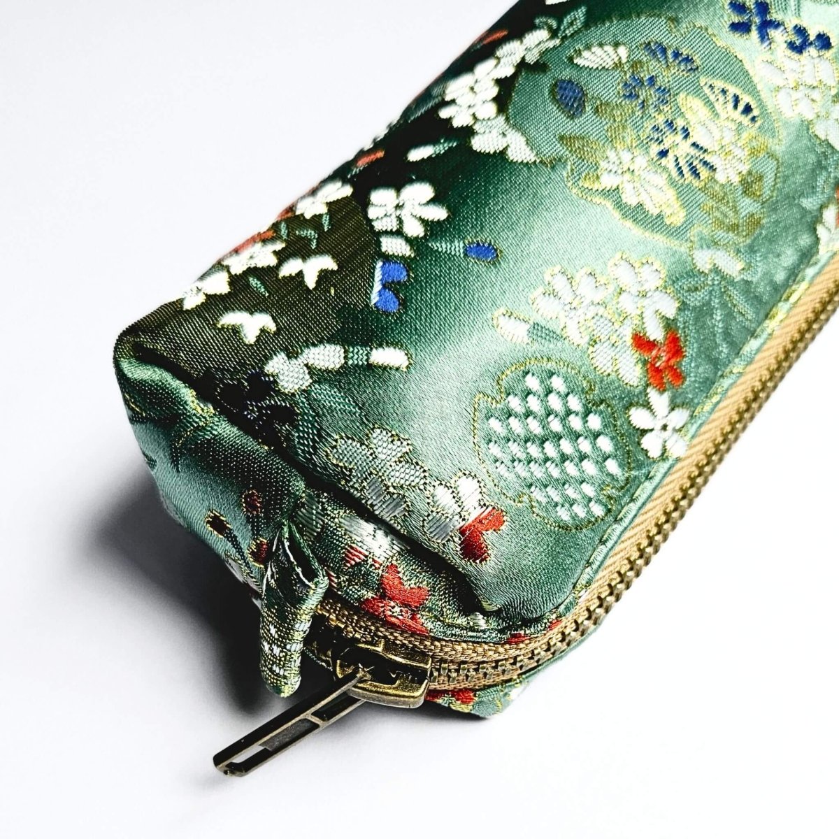 close up detail of embroidery and gold zip on green floral pencil case