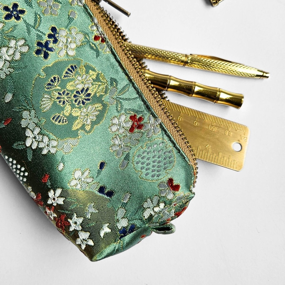 close up of green blossom print pencil case with gold pens inside