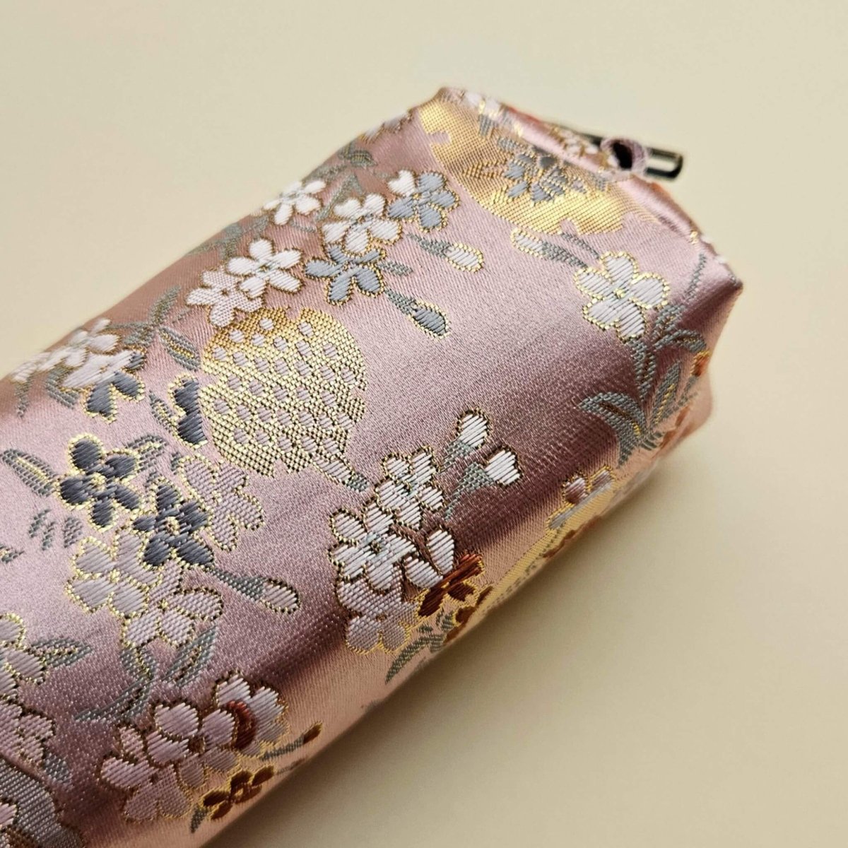 Pink pen pouch with floral embroidery on a beige background