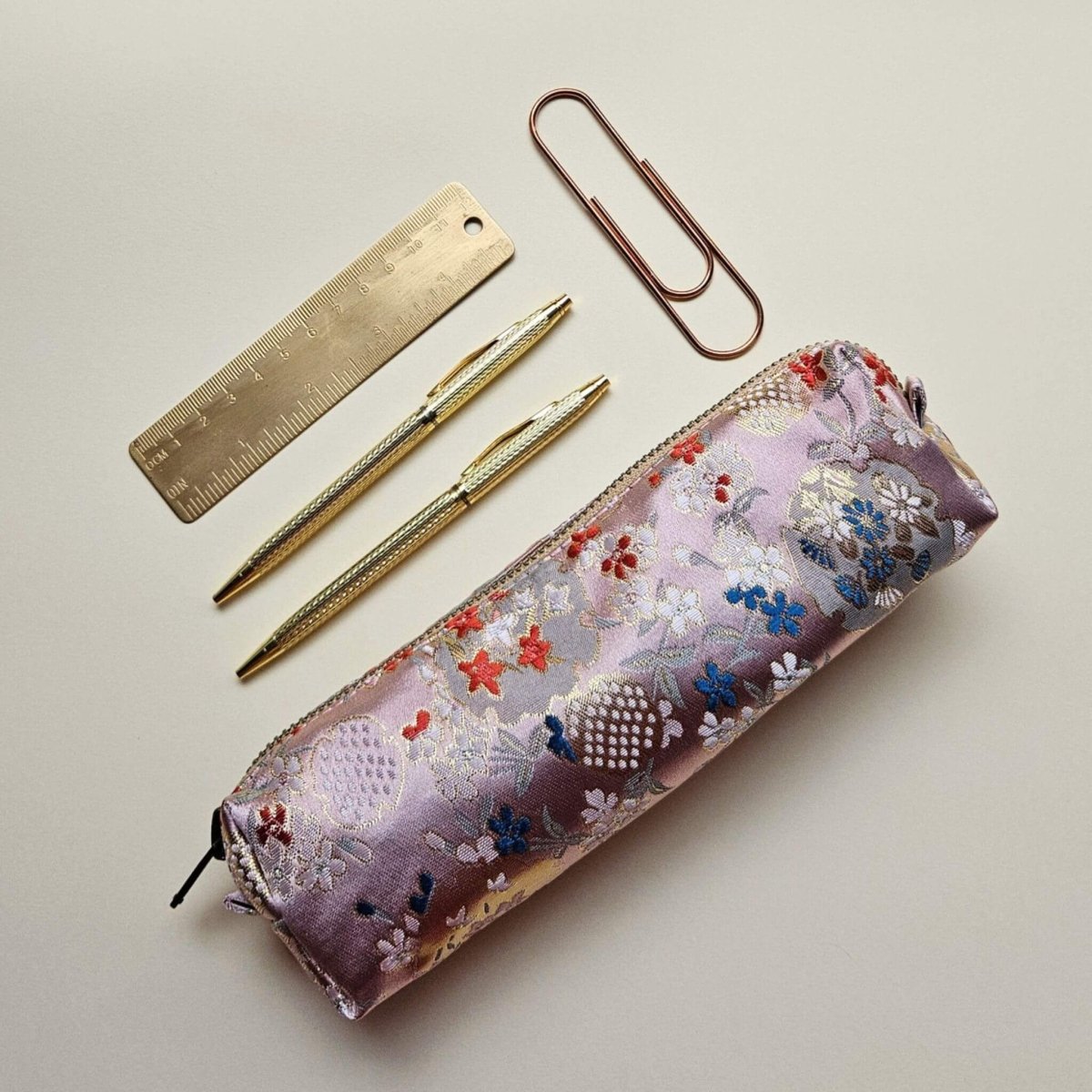 Light pink floral-patterned pencil case with gold pen, ruler, and paper clips on a light background