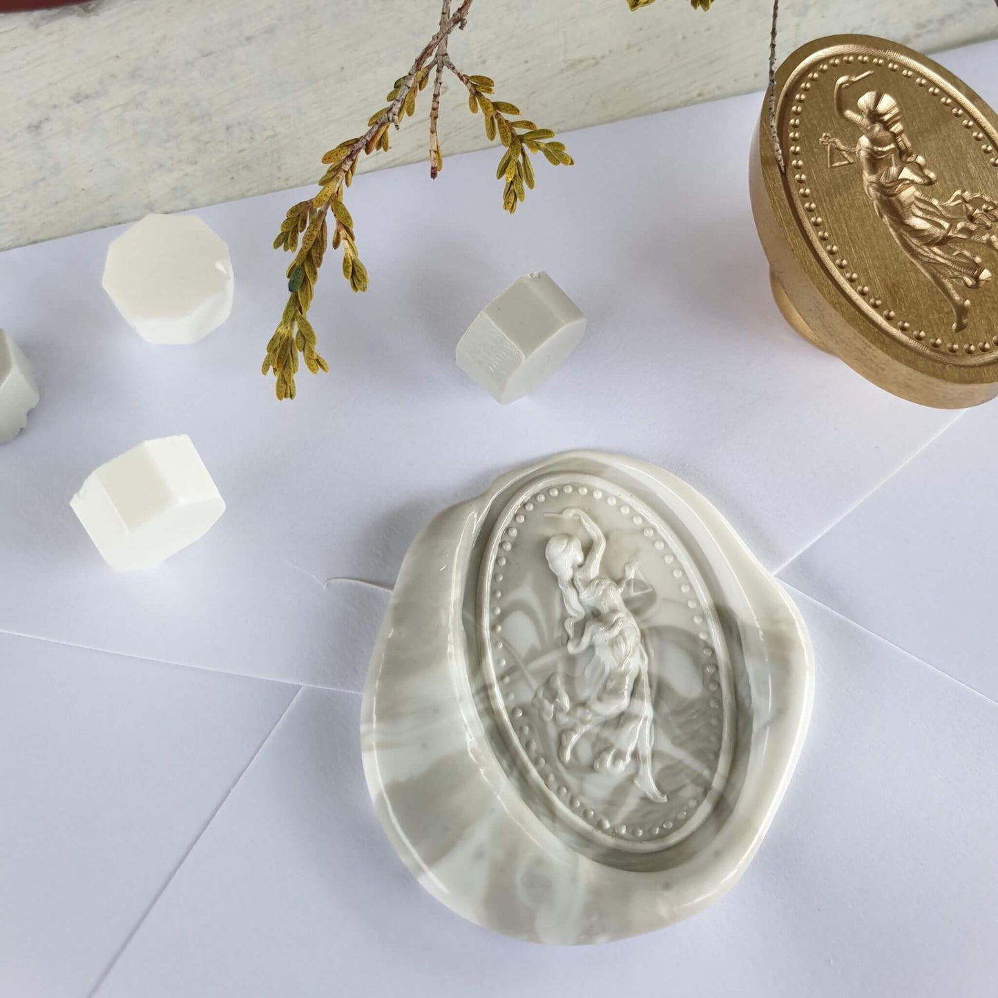 close up of Godess wax seal in marbled grey and white sealing wax with brass wax seal head next to it