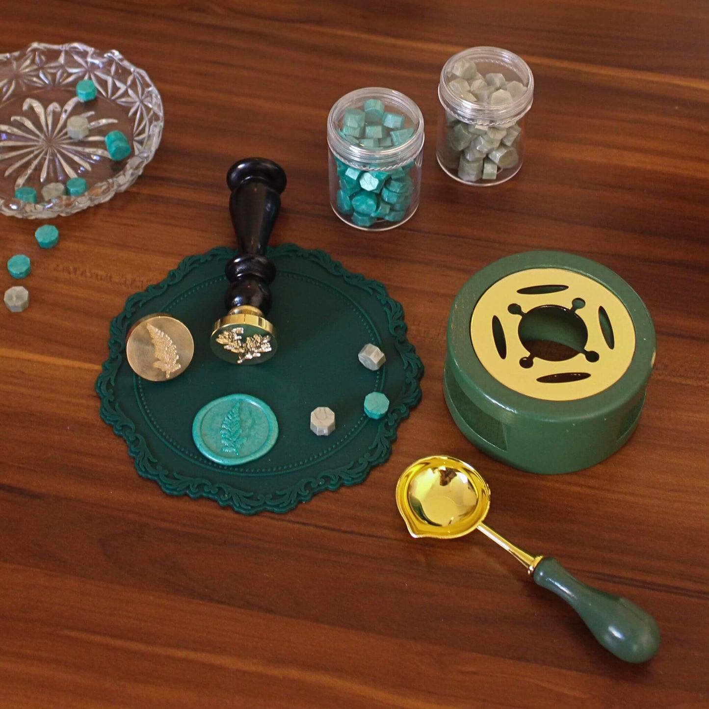 green wax seal kit laid out on desk with green sealing wax, fern and foliage wax seals and wax melting stove and spoon in green