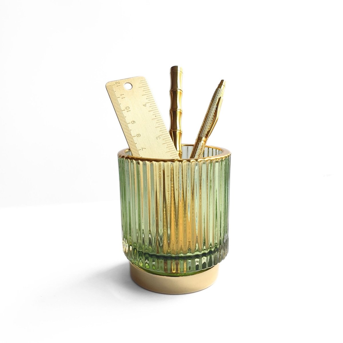 green ribbed glass pen cup holding brass stationery