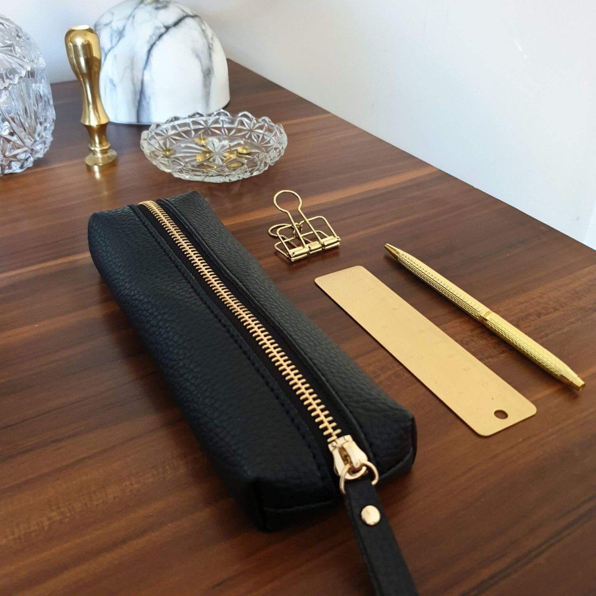 dark brown desk with black and gold pencil case and gold stationery
