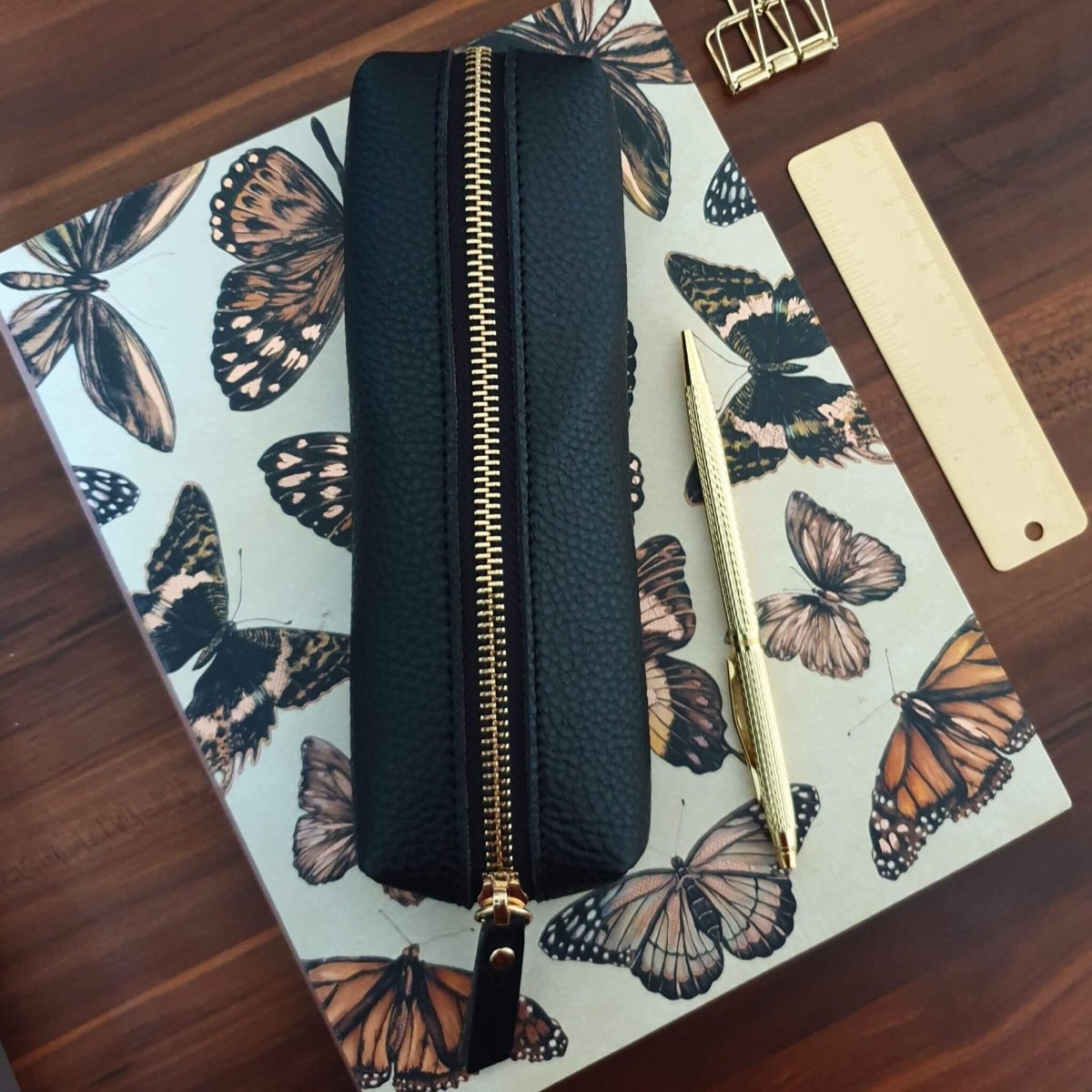 butterfly notebook with black pencil case and gold pen on top.