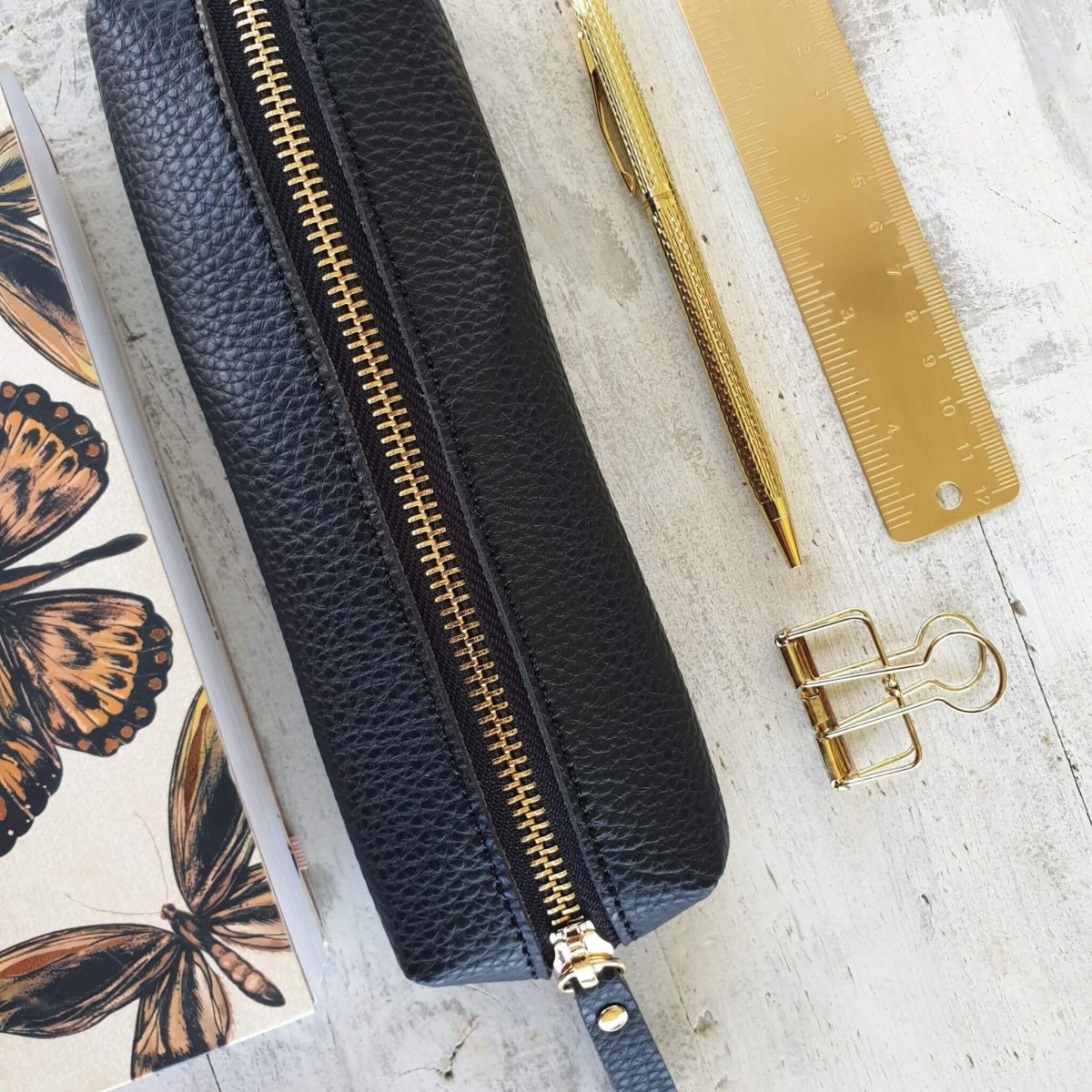 small black pencil case next to gold pen and ruler and notebook