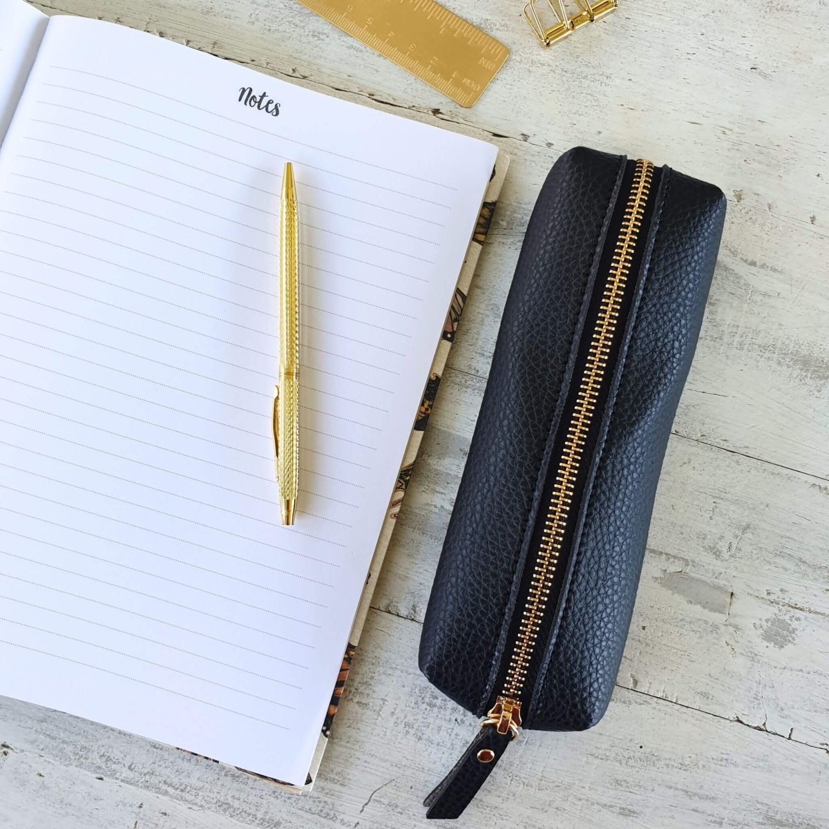 open notebook with black pencil case and gold pen
