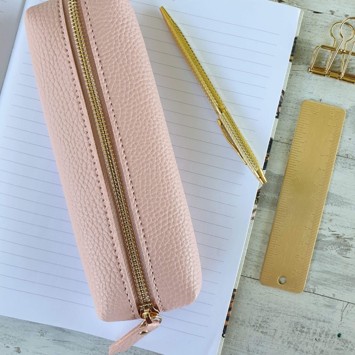 small pink pencil case on notebook with gold stationery