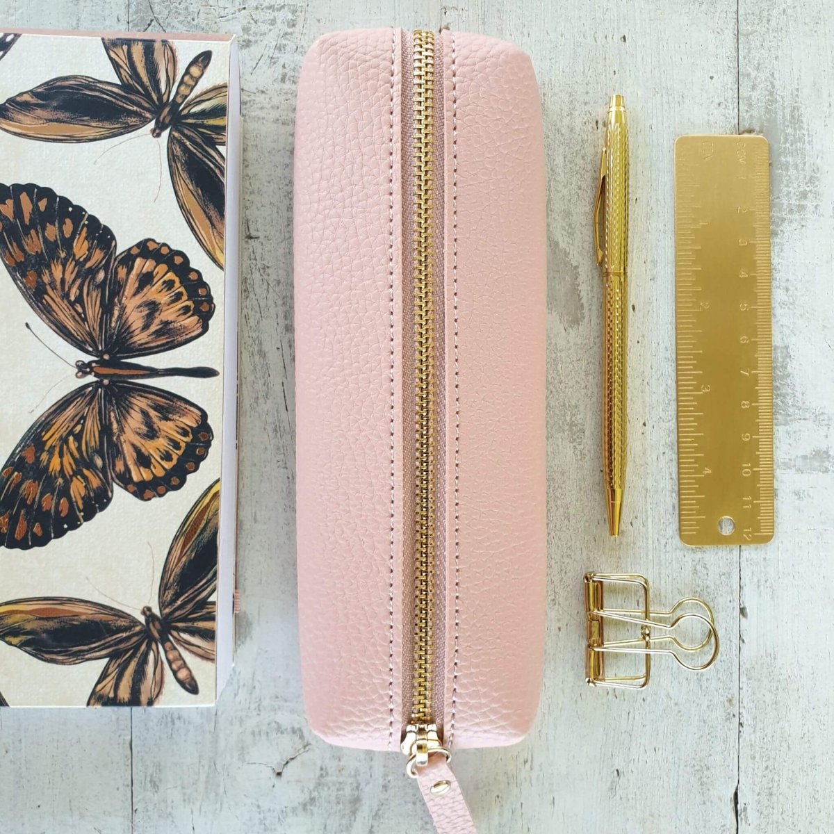 pink pencil case with gold pen, ruler and clip next to notebook