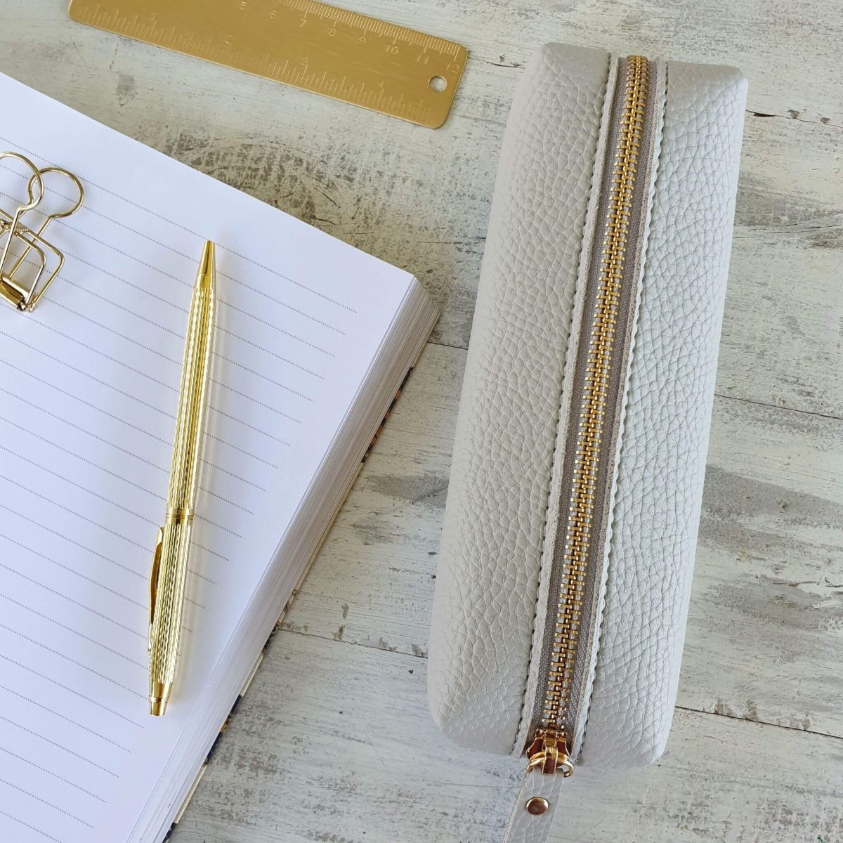small grey pencil case on desk with notebook and gold pen