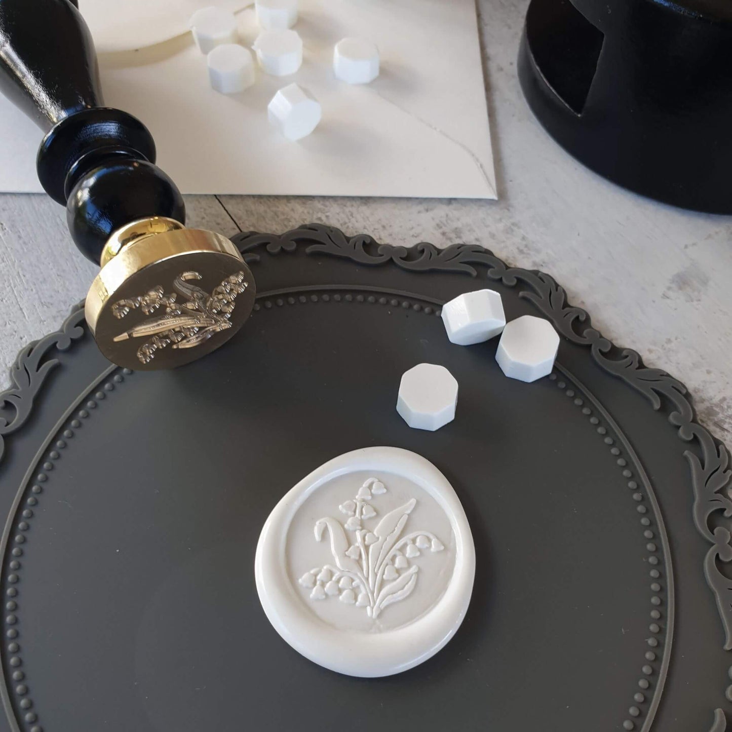 grey rococo wax seling mat in use with wax seal stamp, white floral wax seal and white wax sealing beads