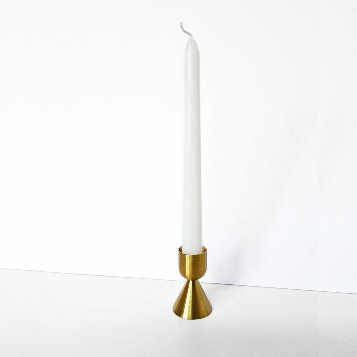 Brass candle holder with a white candle on a white background