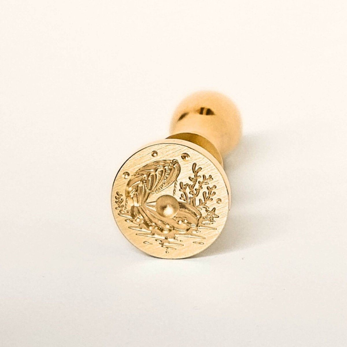 Gold wax seal with a shell design on a white background