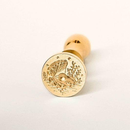 Gold wax seal with a shell design on a white background