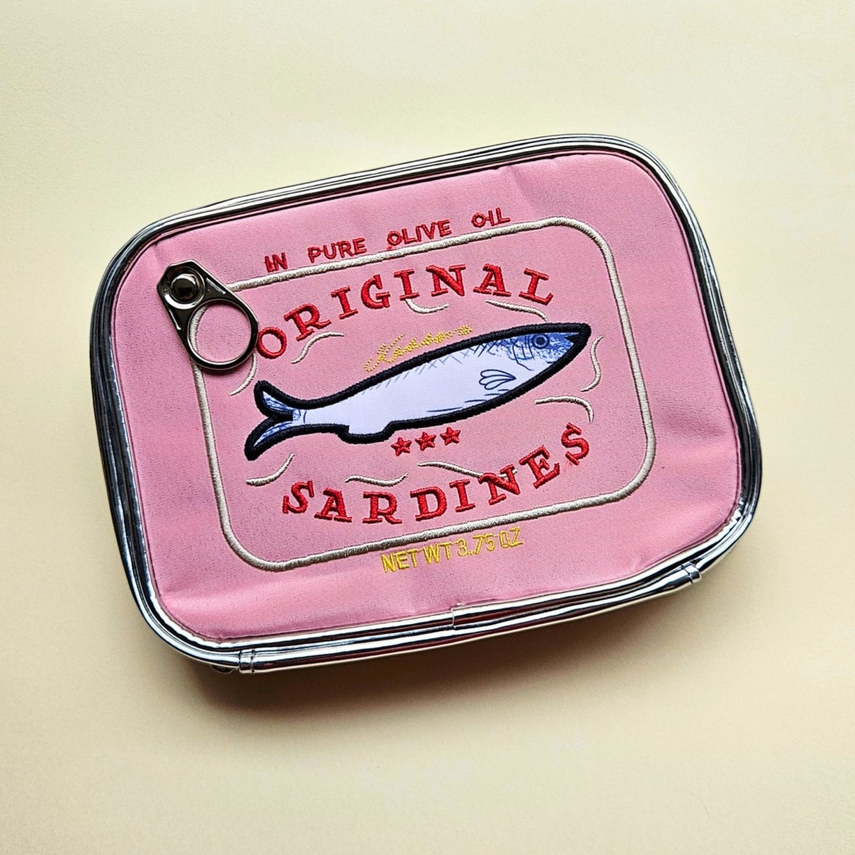 Pink sardine can-shaped pen pouch with 'Original Sardines' text on a beige background