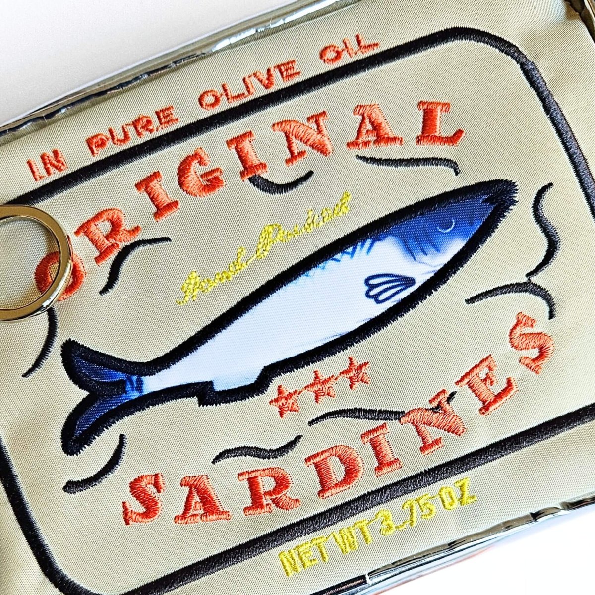 Close up of embroidered label of 'Original Sardines' on a beige pencil case
