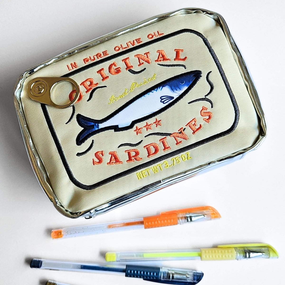 Sardine can-shaped pencil case with pens on a white background