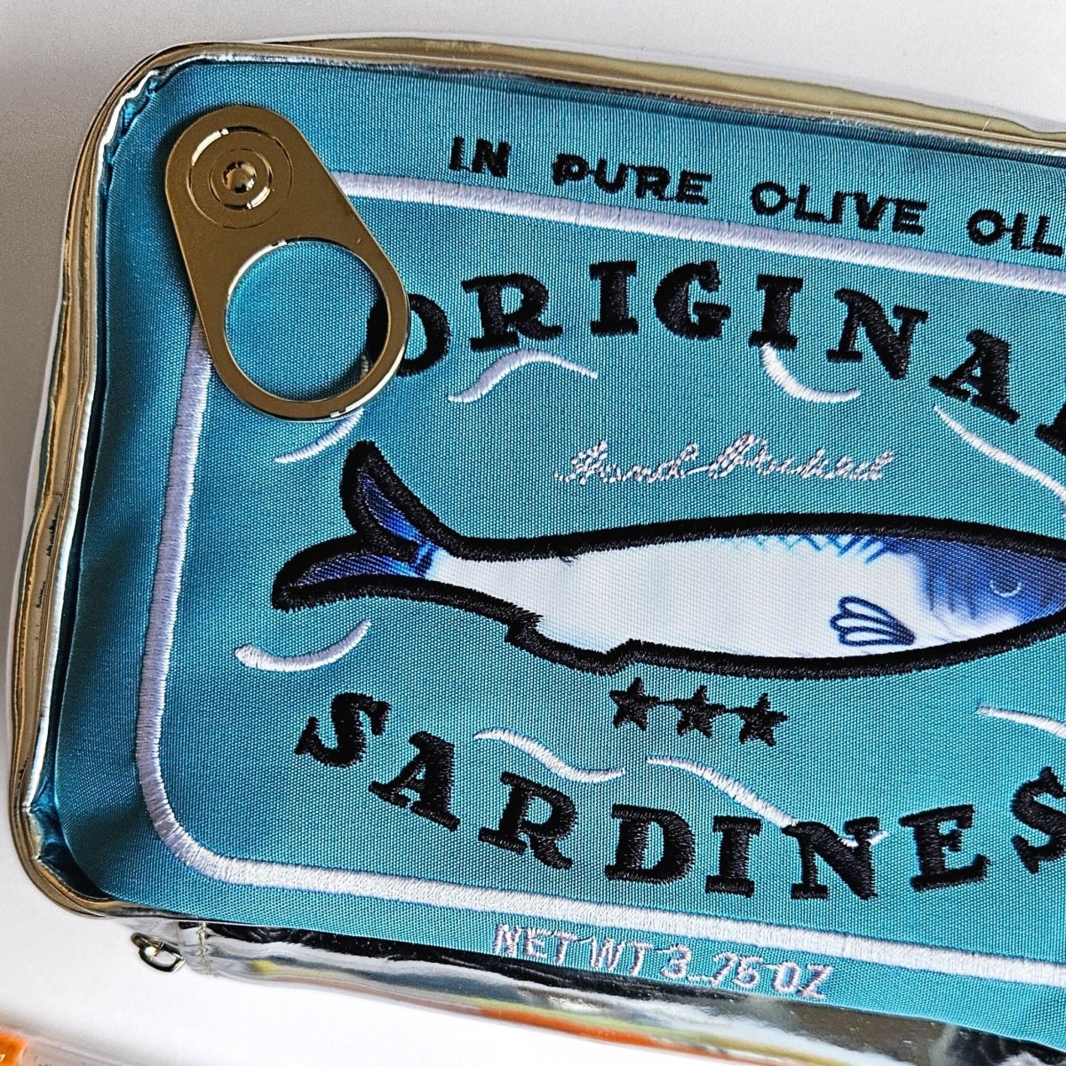Close-up of a sardine tin shaped pencil case with a blue label and fish illustration.