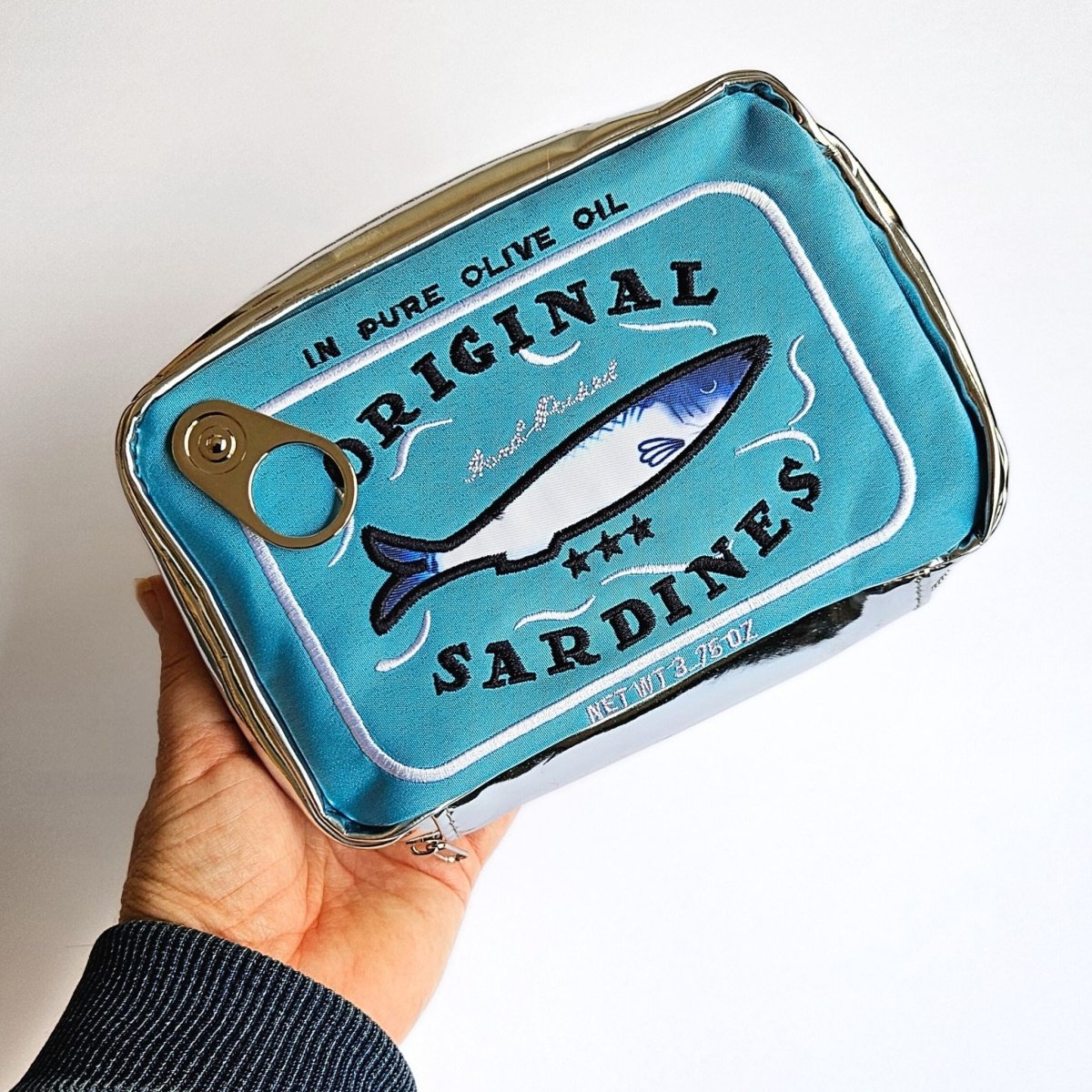Sardine can-shaped pencil case with 'Original Sardines' text and fish illustration on a light blue background.