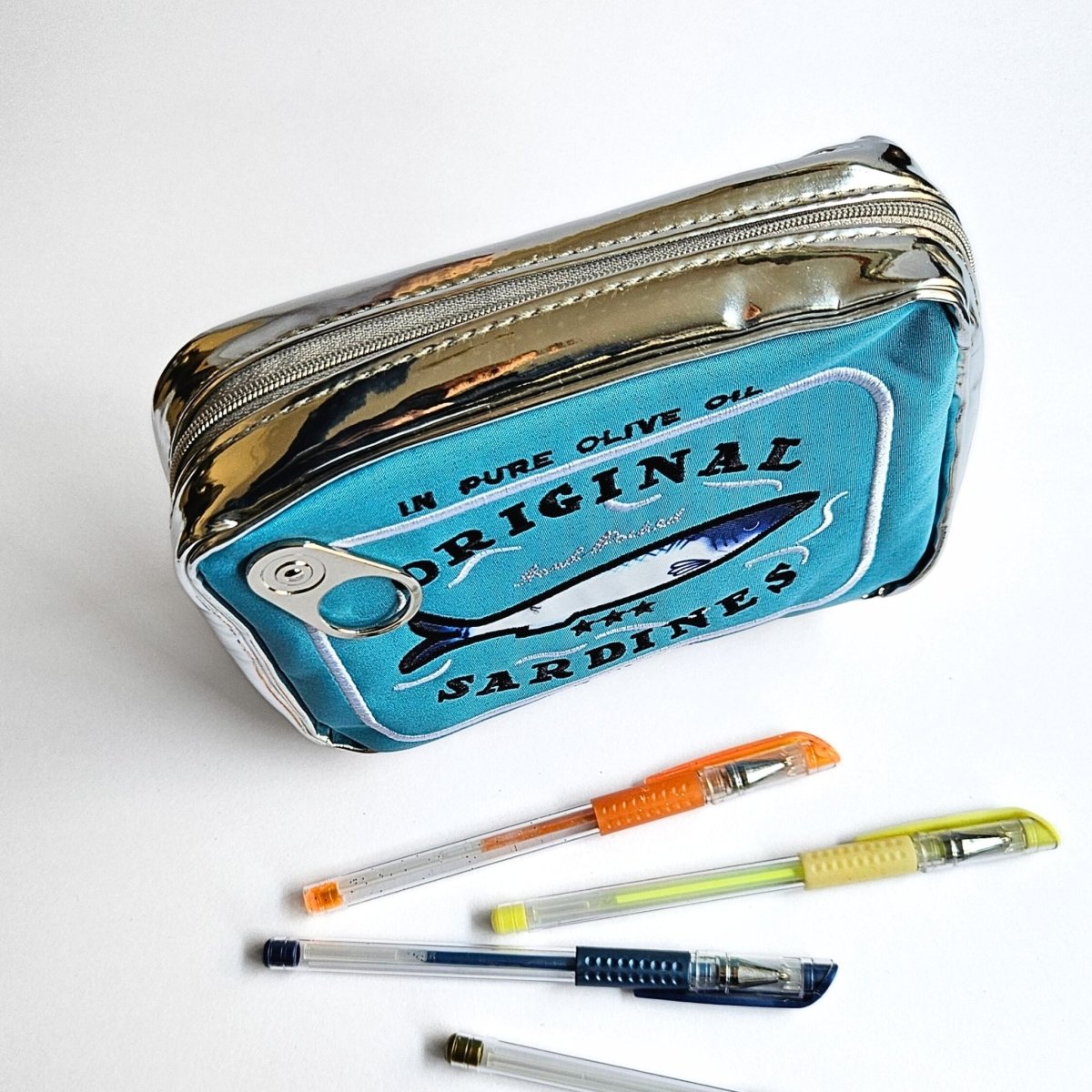 Blue pencil case designed like a sardine can with pens on a white background