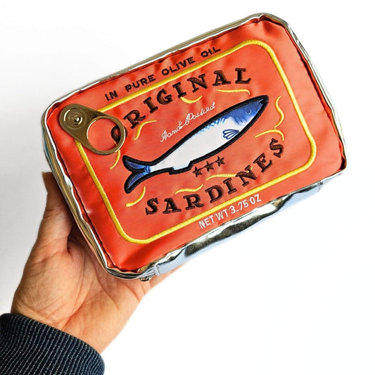 Hand holding an orange-red sardine tin pencil case with a fish illustration on a white background