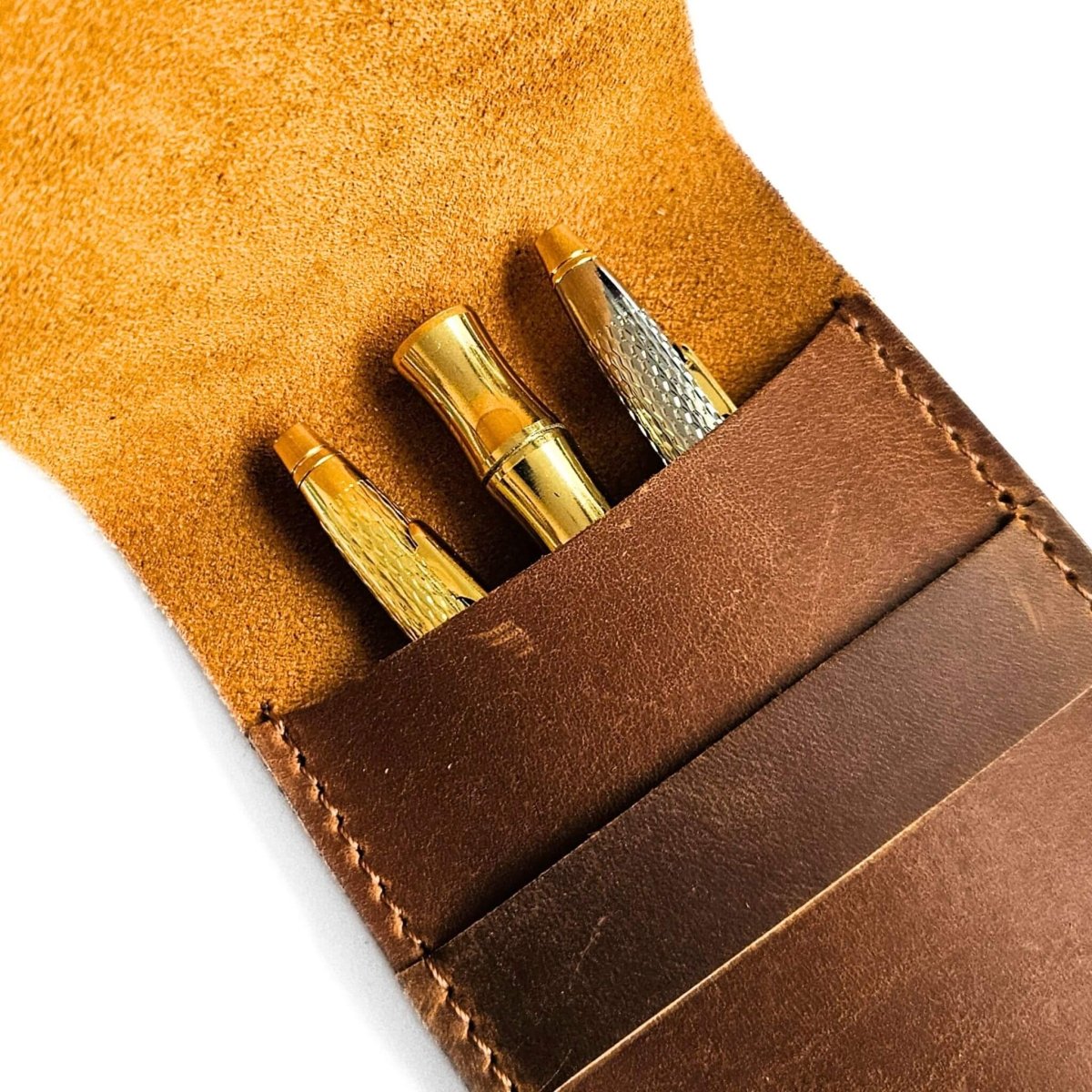 Brown leather pen case open with with three gold pens inside on a white background