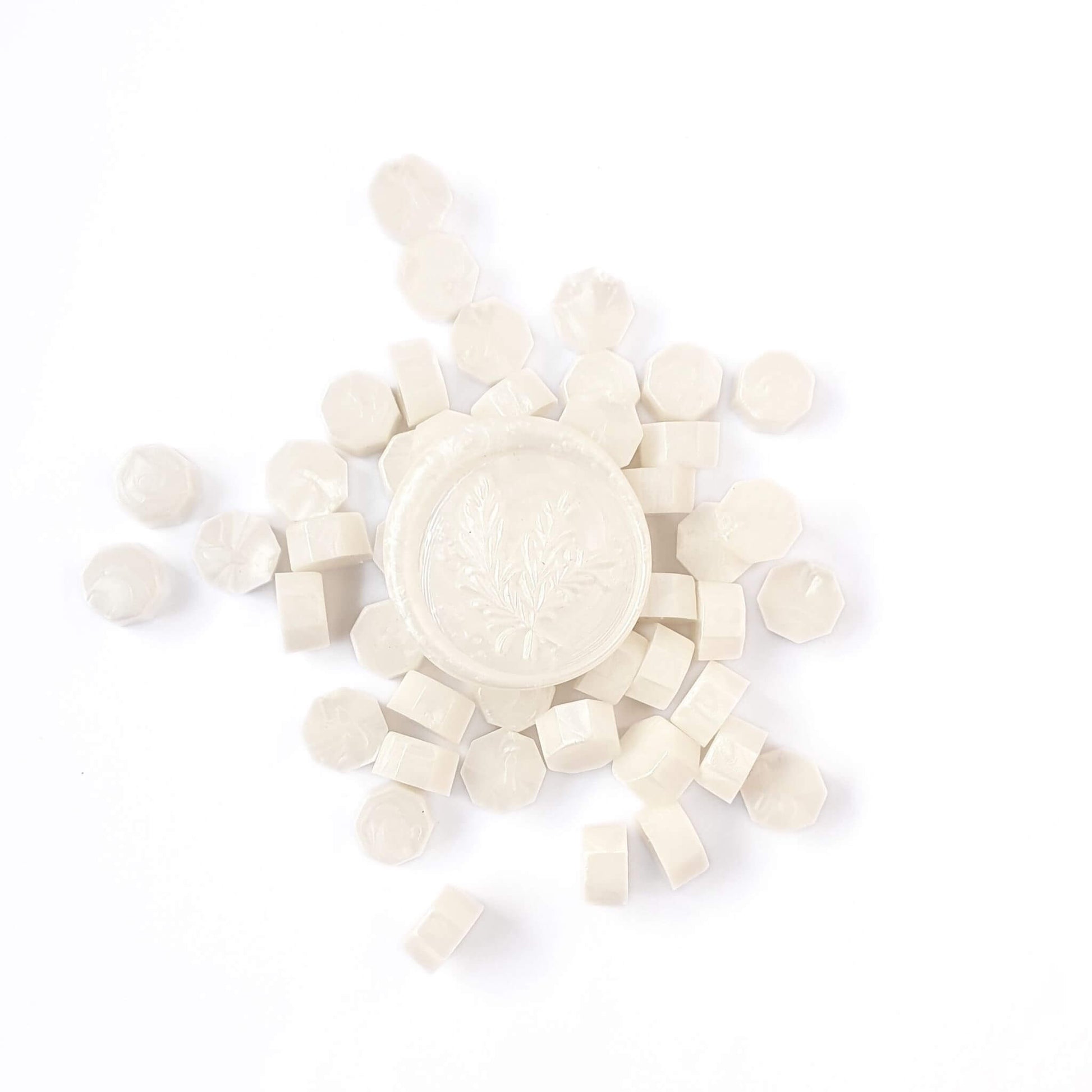 White pearl sealing wax beads in a pile woith a white pearl wax seal in the centre. 
