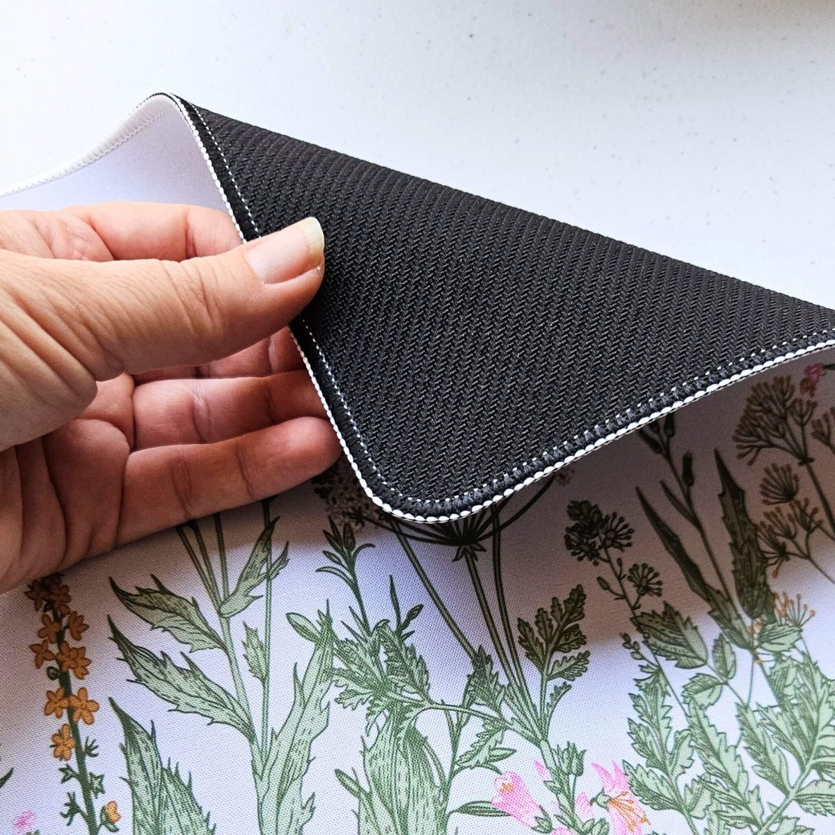 Hand holding floral mouse mat and showing rubber backing